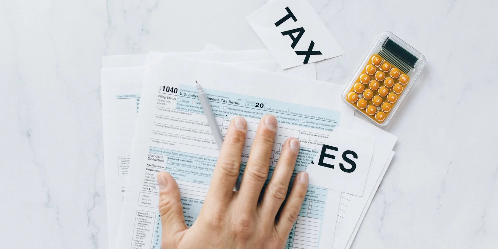 A person filling in printed tax documents at a desk.
