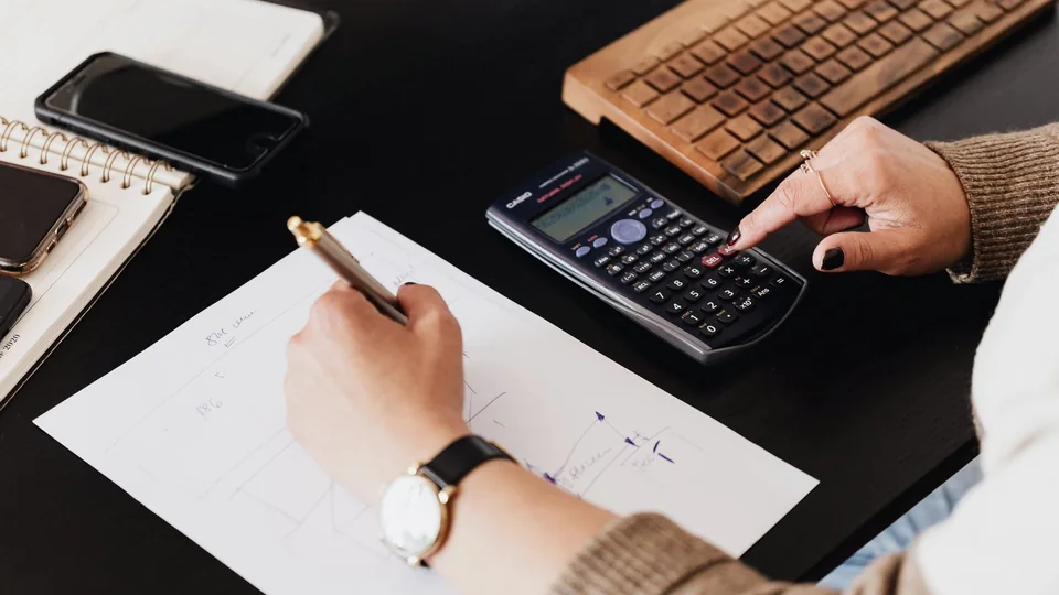 Hands working through a calculation with a calculator and pen.